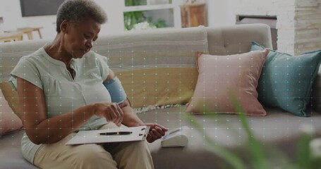 Animation of cardiograph over senior biracial woman taking notes on clipboard - Powered by Adobe
