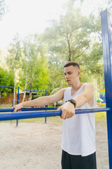 Obraz premium Handsome pumped up young male bodybuilder doing exercises on horizontal bar and parallel bars outdoors on the street. Beautiful male body shapes, beauty and health, training and motivation