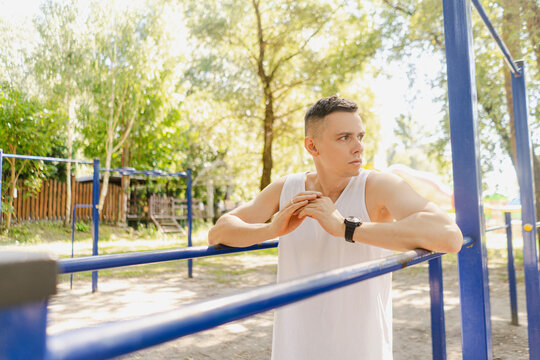 Handsome pumped up young male bodybuilder doing exercises on horizontal bar and parallel bars outdoors on the street. Beautiful male body shapes, beauty and health, training and motivation
