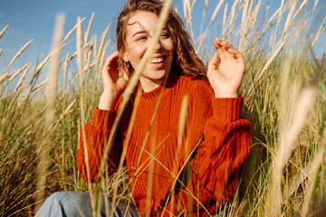 Young woman enjoying a sunny day outdoors in tall grass while wearing a cozy red sweater. Countryside