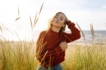 Young woman enjoying a sunny day outdoors in tall grass while wearing a cozy red sweater....