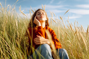 Young woman enjoying a sunny day outdoors in tall grass while wearing a cozy red sweater....
