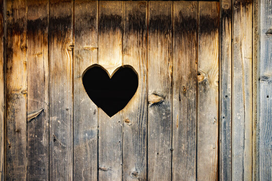 Rustic wooden door with heart-shaped carving, worn texture and natural shades, ideal for rural settings.