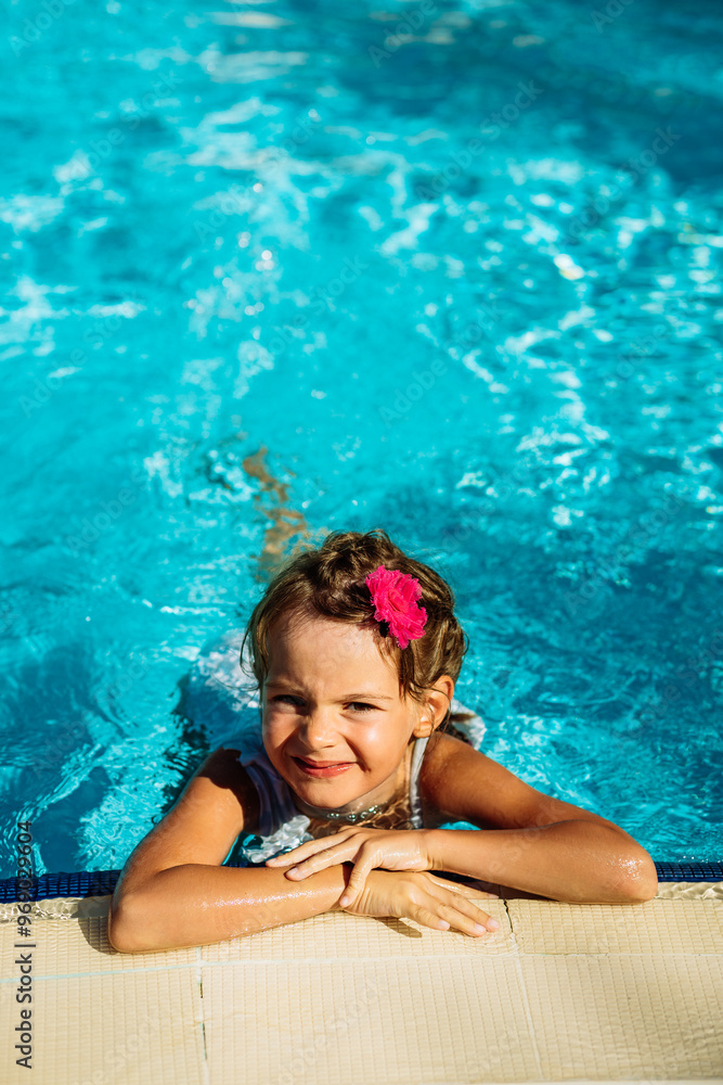 Wall mural a cute happy little girl submerged in a swimming pool up to her shoulders