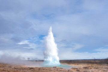 Tourists marvel at the Strokkur geyser erupting, sending a plume of steam and water high into the air. This geothermal wonder is a popular attraction in Iceland. Geysir Geothermal Area, Iceland.