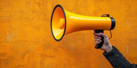 Hand holding bright yellow megaphone on orange background