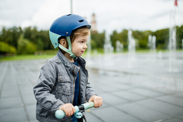 Adorable little boy riding his scooter in a city on sunny autumn evening. Young child riding a...
