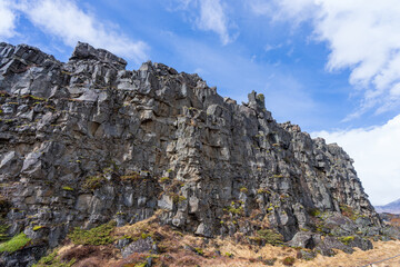 A hiker walks along a trail in Thingvellir National Park, Iceland, with the iconic rift valley between the North American and Eurasian tectonic plates in the background.