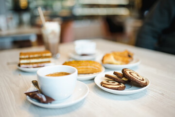 Two cups of cappuccino coffee with various cakes and pastries on a wooden table.