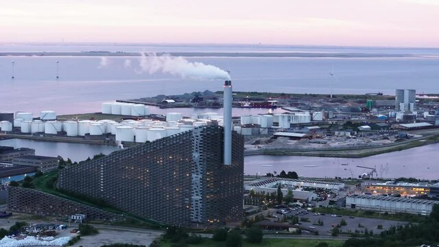 Amager Bakke, a waste to energy facility in Copenhagen, Denmark, releases smoke from its chimney at dusk, showcasing modern architecture and urban sustainability