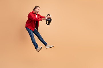 Full length portrait of nice young man jump arms hold wheel wear red shirt isolated on beige color background