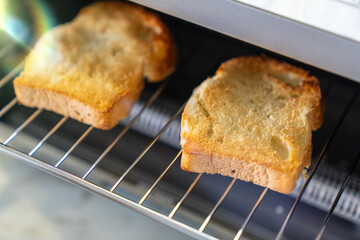 Two slices of golden-brown toast being prepared in a toaster oven. The warm, crispy bread sits perfectly on the wire rack, showcasing a simple yet satisfying morning routine. 