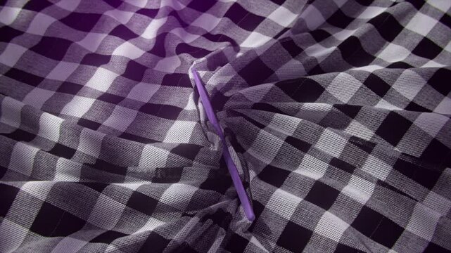Close-up of a black and white checkered fabric with a purple stick inserted into a fold, creating texture and contrast.