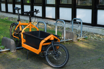 Stylish orange cargo bike parked near modern building on sunny day