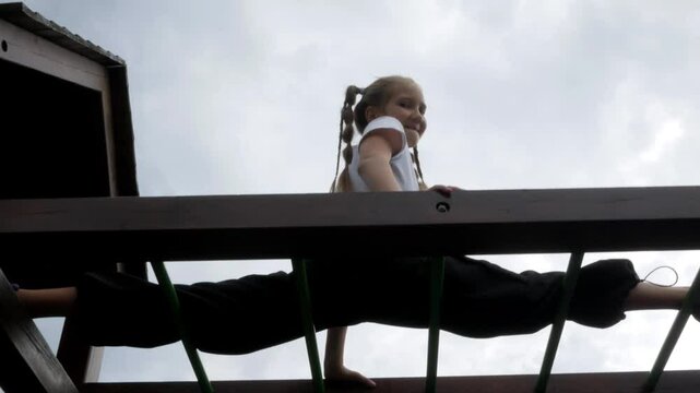Acrobatic gymnast girl does leg stretching on the outdoors sports ground on top. Acrobatic exercise on the horizontal bar and does sports trick splits at height