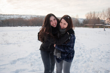 Two women hugging and laughing in the snow, sharing a joyful moment together in a winter field....