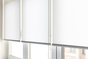 Modern white roller blinds elegantly covering windows in a bright, minimalist room during daylight....