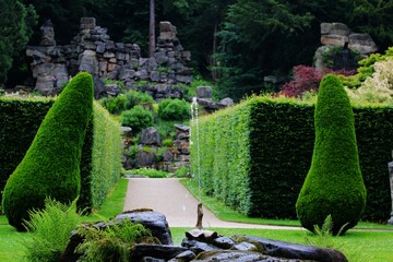 an English castle garden with a pile of stones in the background and a teak with a fountain in the...