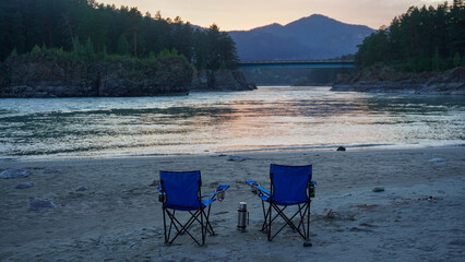 Folding chairs on the bank of a mountain river on a nice, warm day. A calm and quiet place to relax and reflect. Equipment and a tourist's rest.