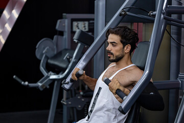 Caucasian man with strong and muscular body training on chest press machine in gym for muscle...