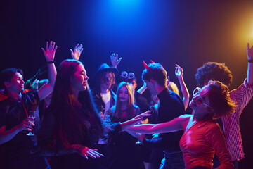 Young people, men and women dressed in themed costumes, with creepy makeup, attending Halloween party at nightclub, dancing, laughing. Concept of Halloween, holiday, party, leisure