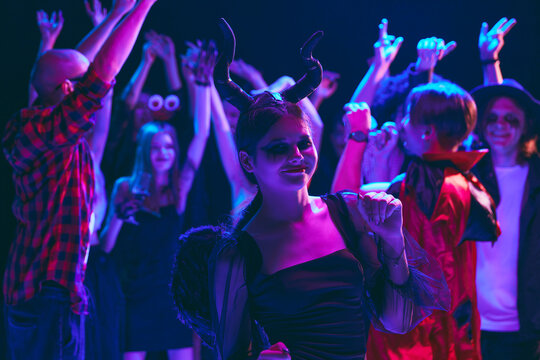 Halloween party scene with cheerful young boys and girls, students wearing various costumes, with creepy makeup, cheerful dancing at nightclub. Concept of Halloween, holiday, party, leisure