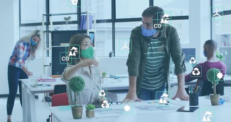 Animation of eco icons over diverse business people wearing face masks in office - Powered by Adobe