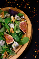 Whole and cut figs with blue cheese, nuts and arugula on a black background. Spicy taste. Mediterranean cuisine.