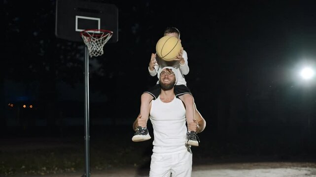Father and son share joyful basketball moments under the night sky in a local park