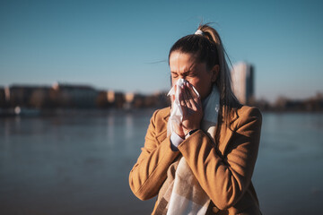 Woman blowing nose while sitting by the river on a sunny winter day. Toned image.	