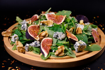 Whole and cut figs with blue cheese, nuts and arugula on a black background. Spicy taste. Mediterranean cuisine.