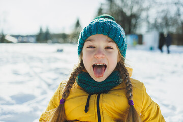 A cheerful girl in a yellow winter coat runs in the snow. A child plays with snowballs in winter. Children's winter entertainment.