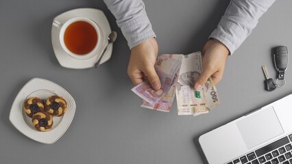 Top view of man at the table counting Ukrainian hryvnias money banknotes and leaving it on the desk, paying bill at cafe or restaurant with cash.