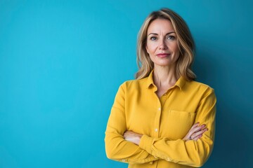 Obraz premium Beautiful, attractive, middle aged woman wearing casual yellow shirt with arms crossed standing isolated on blue background. with generative ai