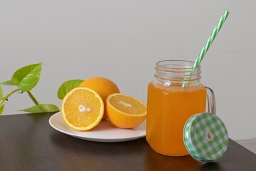 A picture of oranges cut into two pieces and a mason jar full of orange juice kept alongside the plate on a hot sunny day.