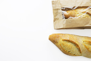 Two freshly baked baguettes, one wrapped in brown paper bag, Artisan French baguettes with crispy crusts in paper packaging. Isolated on a white background. Closeup. With clipping path.