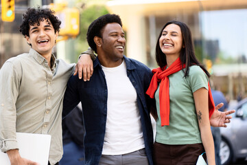 Three young professionals laughing together on busy city street