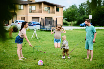 Happy family spending weekend in their backyard jumping rope and playing ball