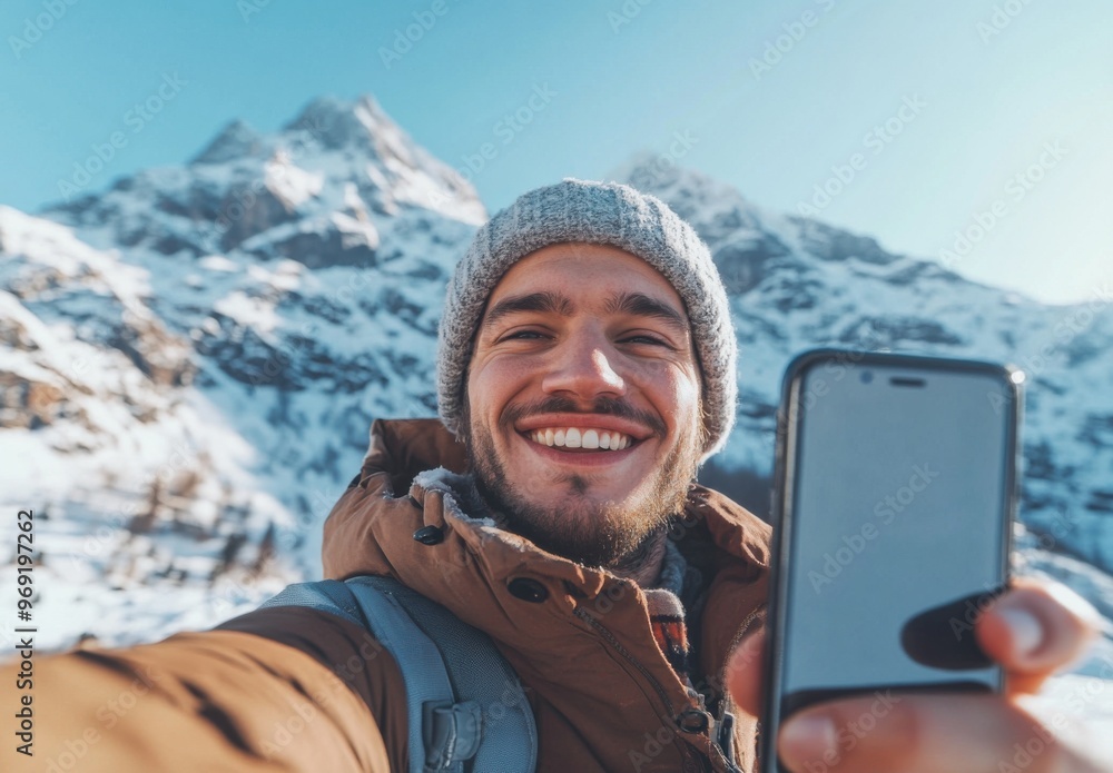 Poster portrait of a smiling man taking a selfie with a mobile phone while hiking in the winter mountains