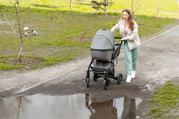 Young mother carefully pushing baby stroller around puddle in park