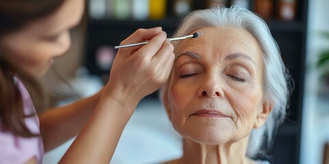A woman has her makeup applied by another.