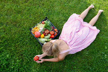 Some of the vegetables are arranged in an interesting way, creating a beautiful composition. Next to the basket lies a young blonde in a striped sundress and long legs.