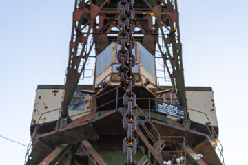 Closeup of a rusty chain on an old industrial harbor crane, highlighting the wear and age of the metal components