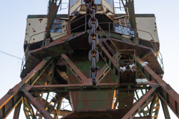 Closeup of a rusty chain on an old industrial harbor crane, highlighting the wear and age of the metal components
