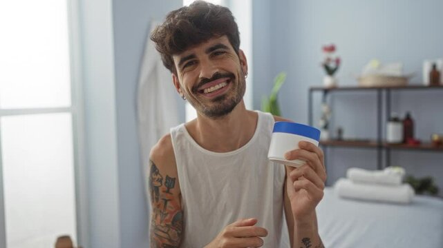 Young man with beard and tattoos enjoying skincare routine with cream in spa wellness room