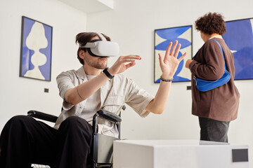 Side view portrait of man with disability using wheelchair and wearing VR tech while interacting with invisible artwork in accessible modern art exhibition copy space