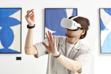 Minimal portrait of man wearing VR headset in modern art museum and while interacting with invisible digital artwork, copy space