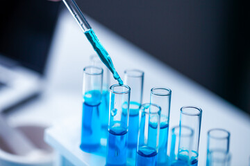 A person is pouring blue liquid into a series of test tubes. The tubes are lined up on a table, and the liquid is being poured into the first one. Concept of precision and scientific experimentation