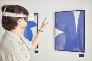 Back view of man wearing Vr in modern art show enjoying interactive mixed reality with paintings,...