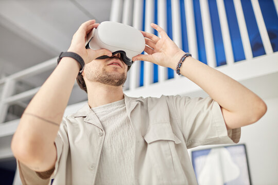 Low angle portrait of man wearing VR headset in modern art museum and looking at digital artwork, copy space